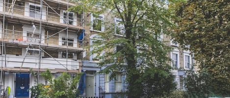 A residential building with a blue door, a tree in front, and a parked car.