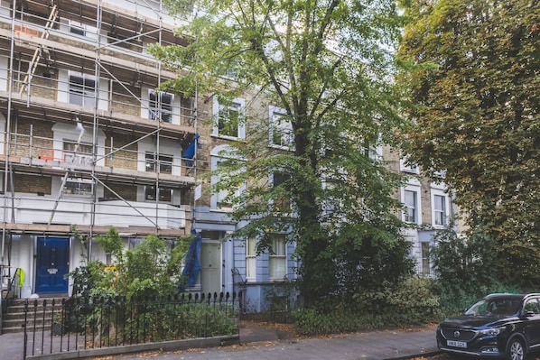 A residential building with a blue door, a tree in front, and a parked car. - Stylish North Kensington One-Bed (London)