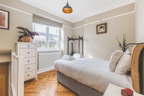 Een slaapkamer met een bed, linnenkast, radiator, raam en kledingrek.