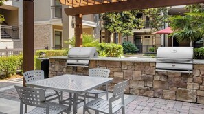 Eine Terrasse im Freien mit zwei Grillstationen, einer Steinmauer und einem Tisch mit Stühlen.
