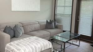 A modern living room with a sectional sofa, a glass coffee table, and a large abstract painting on the wall.