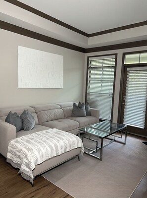 Una sala de estar moderna con un sofá seccional, una mesa de centro de vidrio y un cuadro abstracto grande en la pared.