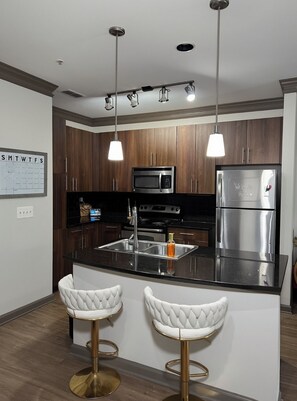 Una cocina moderna con armarios de madera, electrodomésticos de acero inoxidable, una encimera negra y dos taburetes blancos.