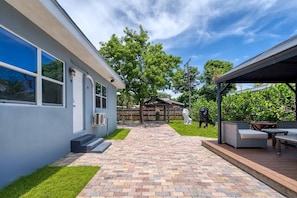 A modern house with a paved patio, a covered outdoor seating area, and a fenced backyard. - Spacious 3BR Hollywood Home, Backyard & BBQ, Close to Beach & Hard Rock (Hollywood)