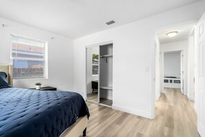 A bedroom with a bed, a window with blinds, a closet with a mirror, and a hallway leading to another room. - Spacious 3BR Hollywood Home, Backyard & BBQ, Close to Beach & Hard Rock (Hollywood)