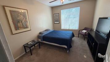 A bedroom with a bed, a ceiling fan, a television, a window with blinds, and a framed picture on the wall.
