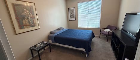 A bedroom with a bed, a ceiling fan, a television, a window with blinds, and a framed picture on the wall.