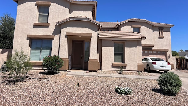A two-story house with a garage, a driveway, and a small garden area with rocks and plants. - Goodyear 2 Story (Goodyear)
