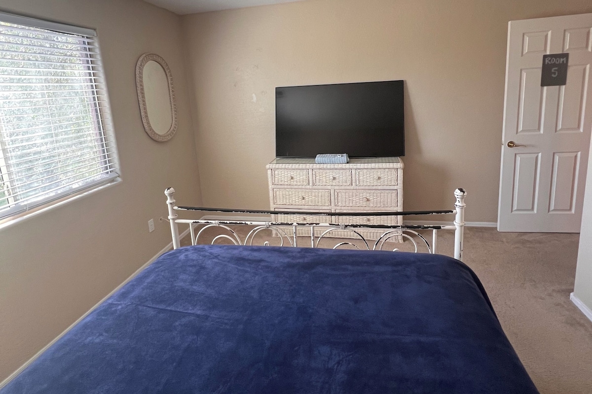 A bedroom with a bed, a dresser, a television, and a door labeled 'ROOM 5'.