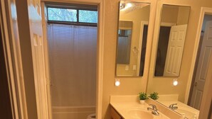 A bathroom with a double sink, wooden cabinets, a mirror, and a window. - Goodyear 2 Story (Goodyear)