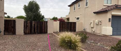 A residential area with a gravel driveway, a wooden fence, and a building with a tiled roof.