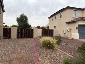 A residential area with a gravel driveway, a wooden fence, and a building with a tiled roof.