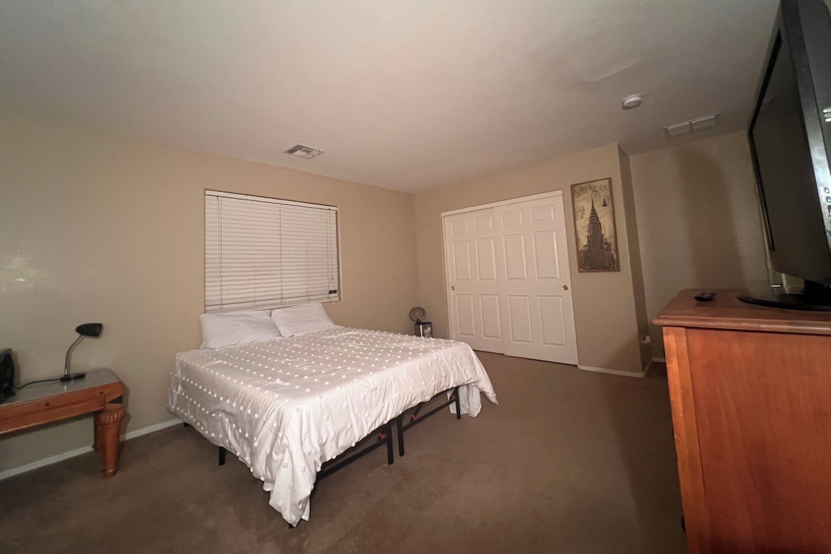 A bedroom with a bed, a desk, a television, and a door.