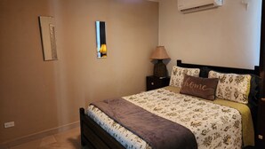 Et soveværelse med seng, natbord, lampe, loftventilator og aircondition.