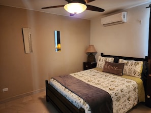 Un dormitorio con cama, mesita de noche, lámpara, ventilador de techo y aire acondicionado.