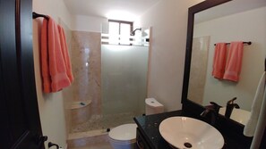 Un baño con ducha, inodoro, lavamanos y un espejo grande.