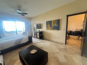 A hotel room with a bed, a desk, a television, artwork on the wall, and a view of the outdoors.