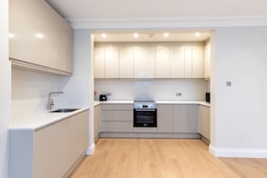 A modern kitchen with white cabinetry, a built-in oven, and a stainless steel sink. - Pimlico 2-Bed | Victoria & Belgravia (London)