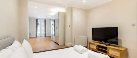 A hotel room with a large bed, a television, a mirror, and a view of the hallway.