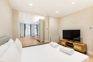 Een hotelkamer met een groot bed, een televisie, een spiegel en uitzicht op de gang.