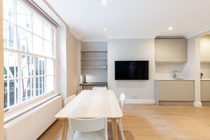 Een moderne keuken met een flatscreen televisie, een eethoek met een houten tafel en stoelen, en een groot raam met zonwering.
