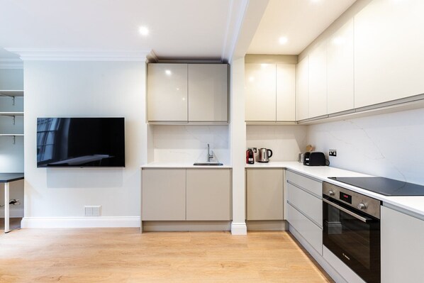 Een moderne keuken met witte kastjes, een inbouwoven en een flatscreen televisie aan de wand.