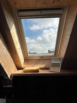 A skylight window with a view of the sky and clouds, a cushion, and a framed picture on a wooden ledge. - SMALL STONE & WOOD HOUSE (Blainville-sur-Mer)