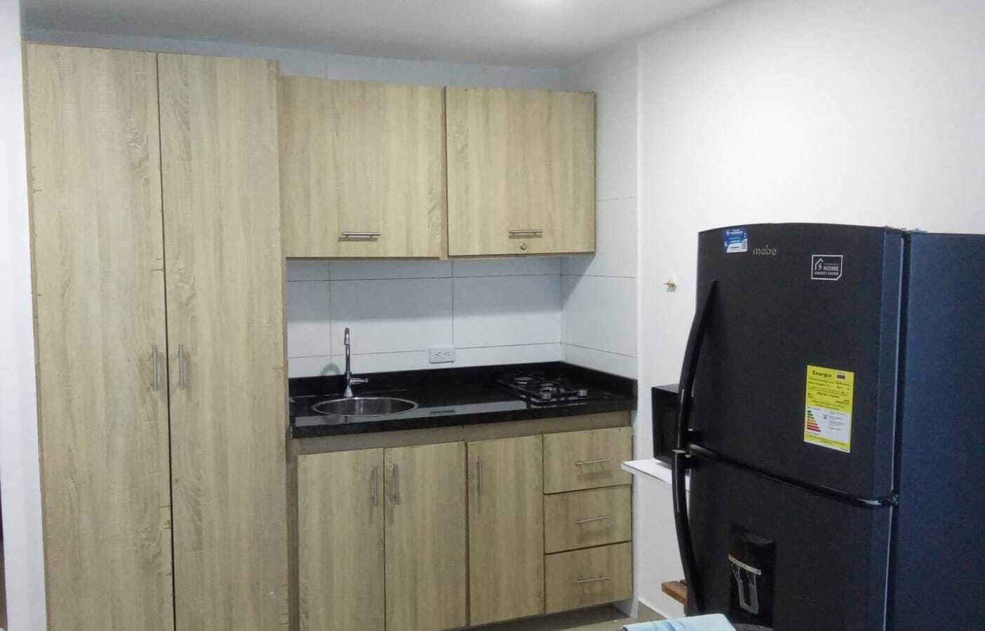 A compact kitchen with wooden cabinets, a black countertop, and a black refrigerator.