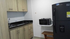 A compact kitchen with a microwave on a shelf, a sink, and wooden cabinets. - Studio 1309—perfect for 2 or 4 people (Cartagena de Indias)