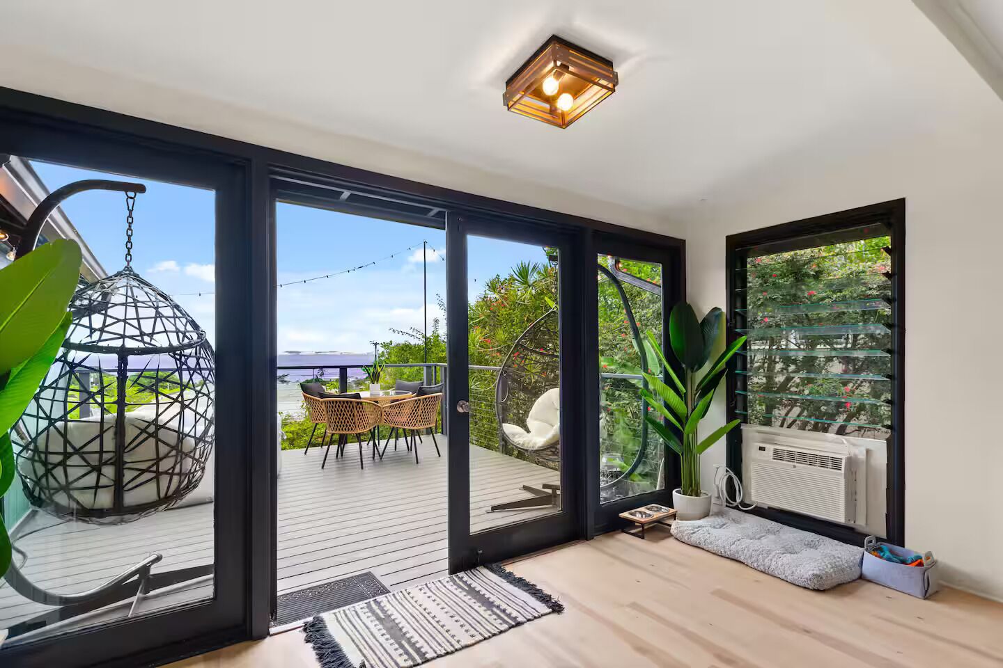 A modern interior with a large sliding glass door leading to an outdoor deck, a hanging chair, and a potted plant.