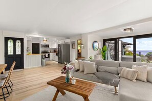 Ein modernes Wohnzimmer mit einer Couch, einem Couchtisch und Blick auf die Küche und den Balkon.