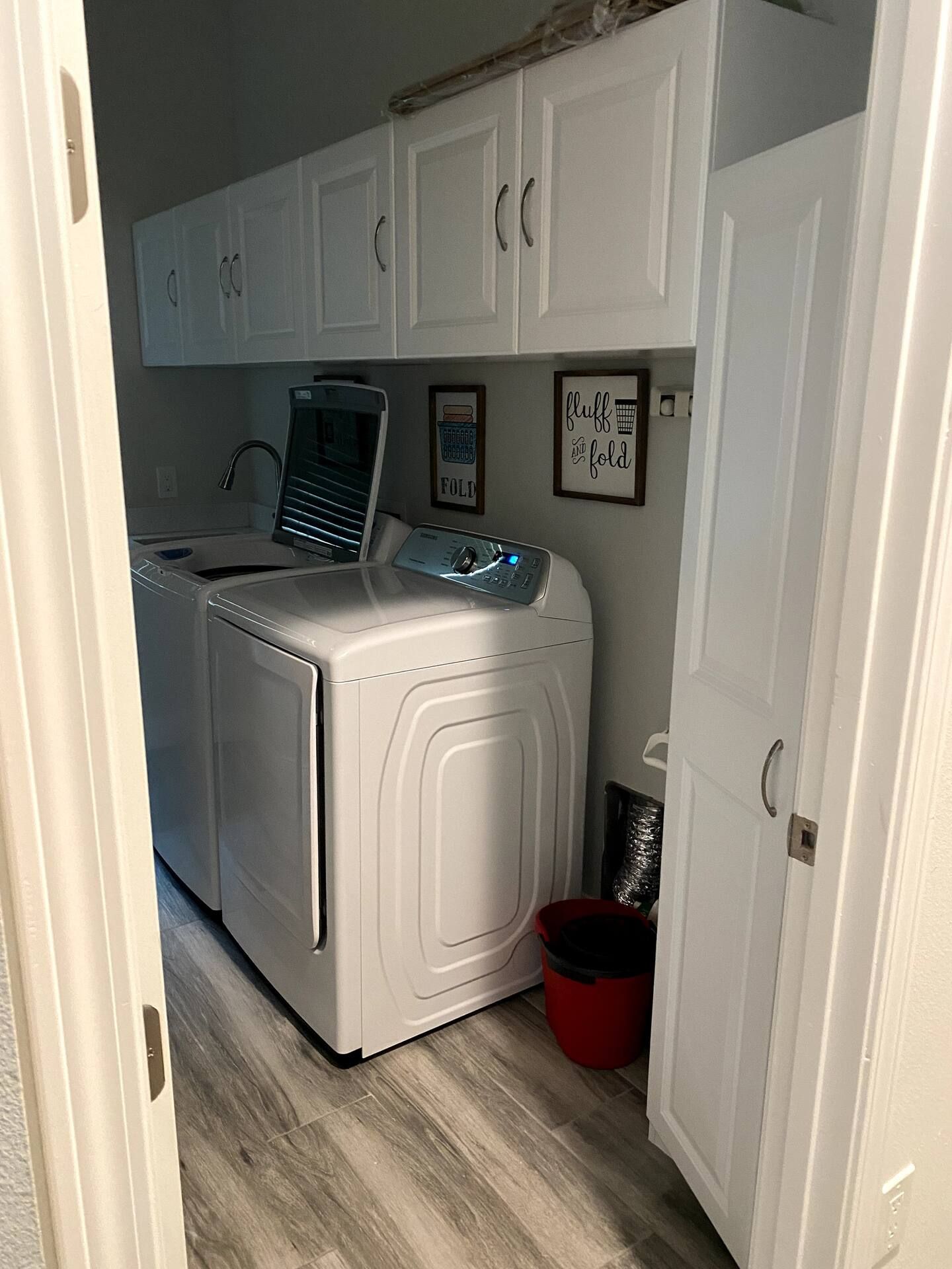 A laundry room with a front-loading washer and dryer, a red bucket, and a wall-mounted drying rack.