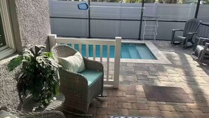 A patio with a pool, wicker furniture, and a white fence.