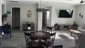 A modern living room with a dining area, a flat-screen TV mounted on the wall, and a ceiling fan.