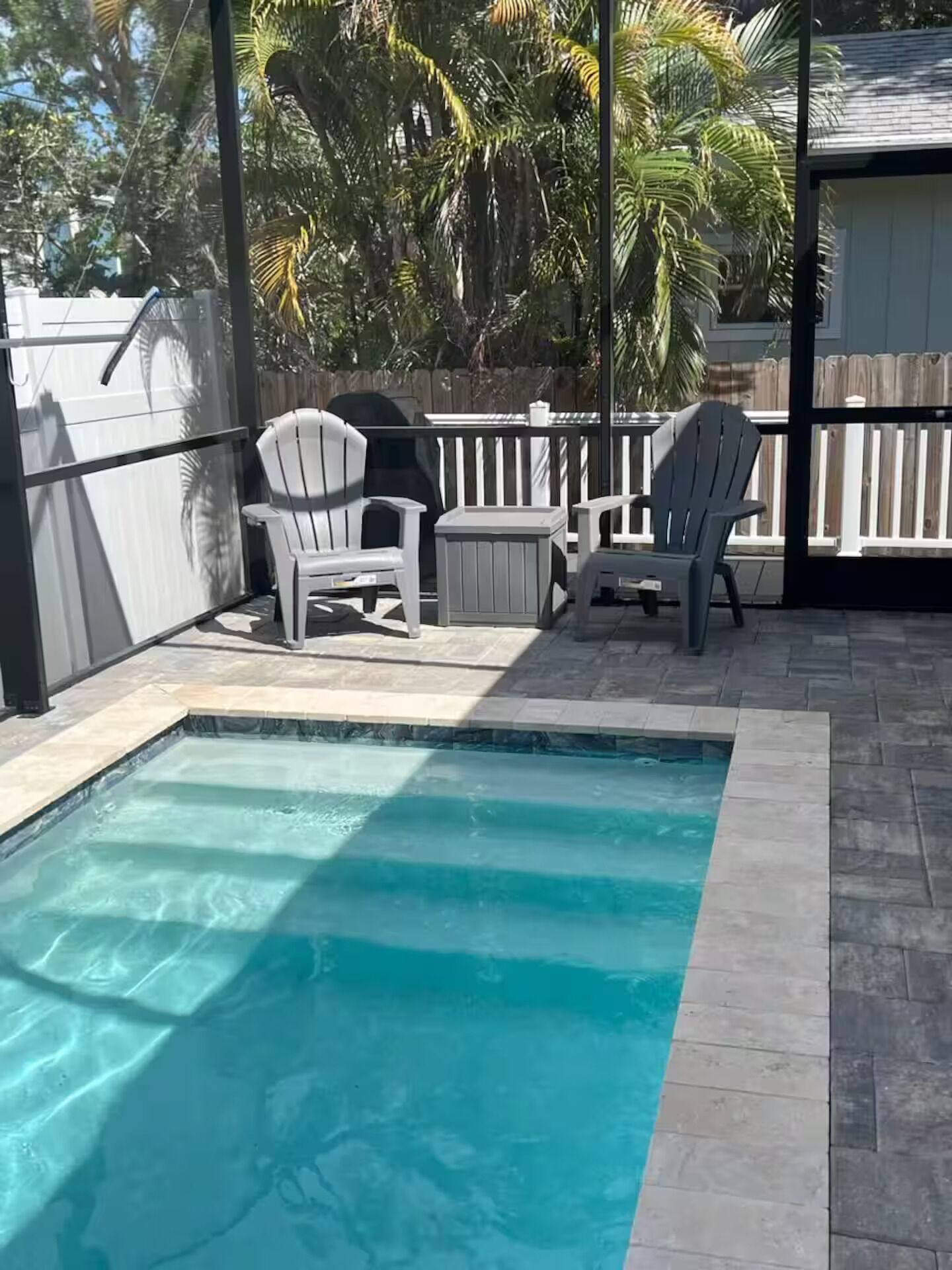A swimming pool with two Adirondack chairs and a wooden fence in the background.