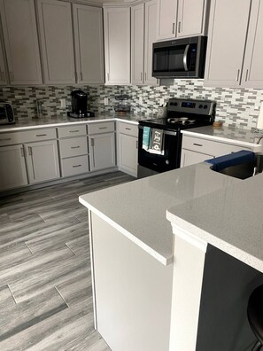 A modern kitchen with white cabinetry, a microwave, a coffee maker, and a stove.