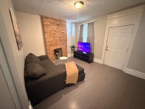Ein Wohnzimmer mit Kamin aus Ziegelsteinen, einem Sofa, einem Fernseher auf einem Schrank und einer Tür.