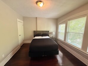 Une chambre à coucher avec un lit, une table de chevet, une lampe et de grandes fenêtres.