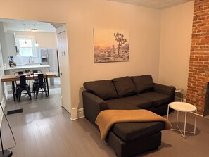 Un salon avec un canapé de couleur sombre, une petite table d’appoint blanche et un tableau représentant un paysage désertique accroché au mur.