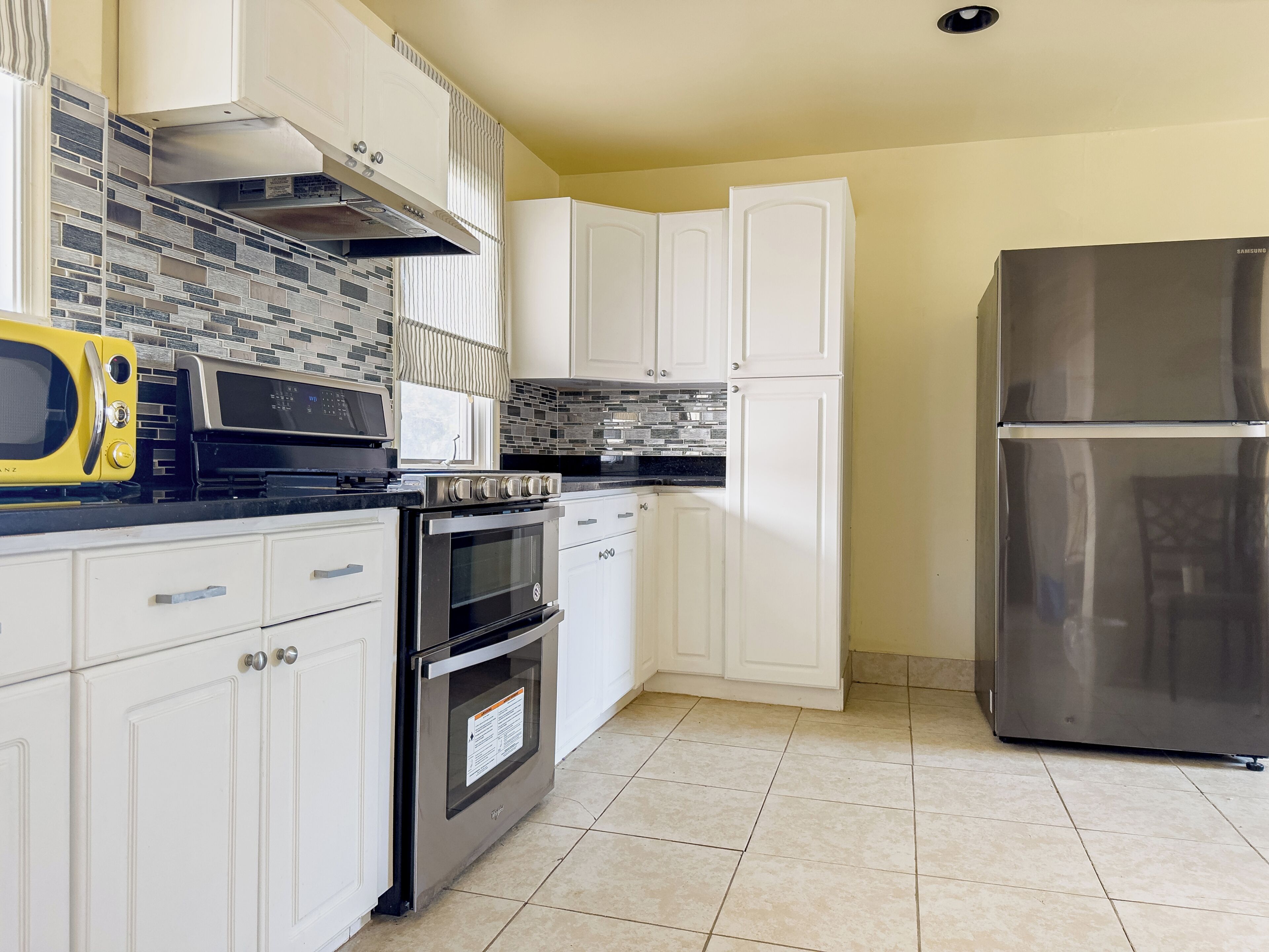 A kitchen with white cabinets, a stainless steel refrigerator, a microwave, and an oven.