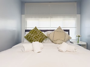 A neatly made bed with two pillows, a white vase with flowers, and a small bedside table.