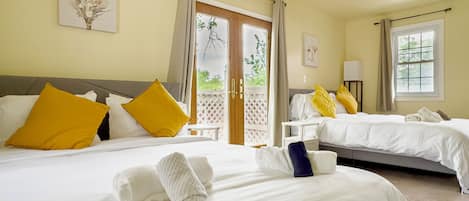 A hotel room with two beds, each with white bedding and yellow pillows. There are towels on the beds, and a window with curtains.