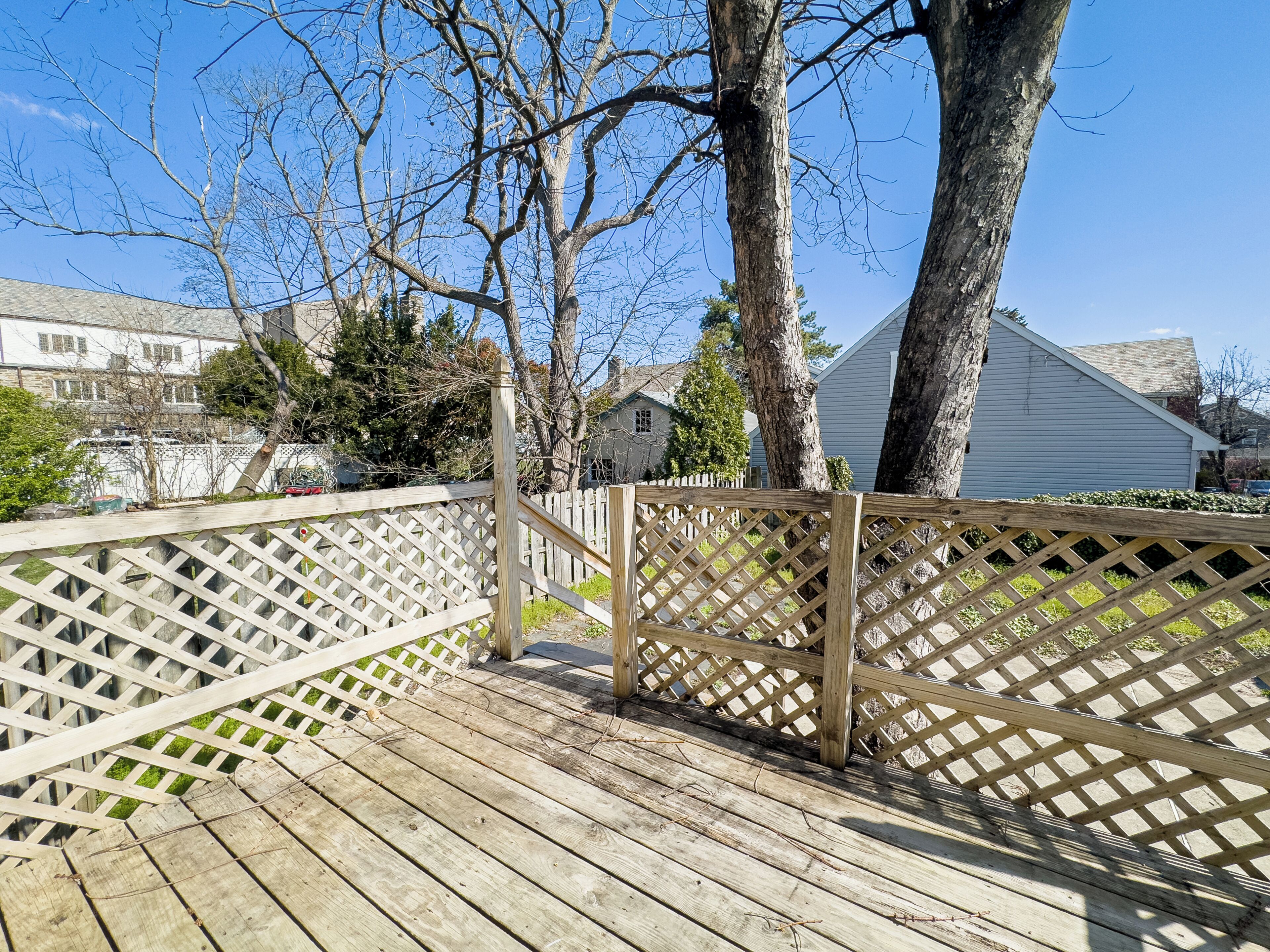 A wooden deck with a lattice fence, surrounded by trees and houses.