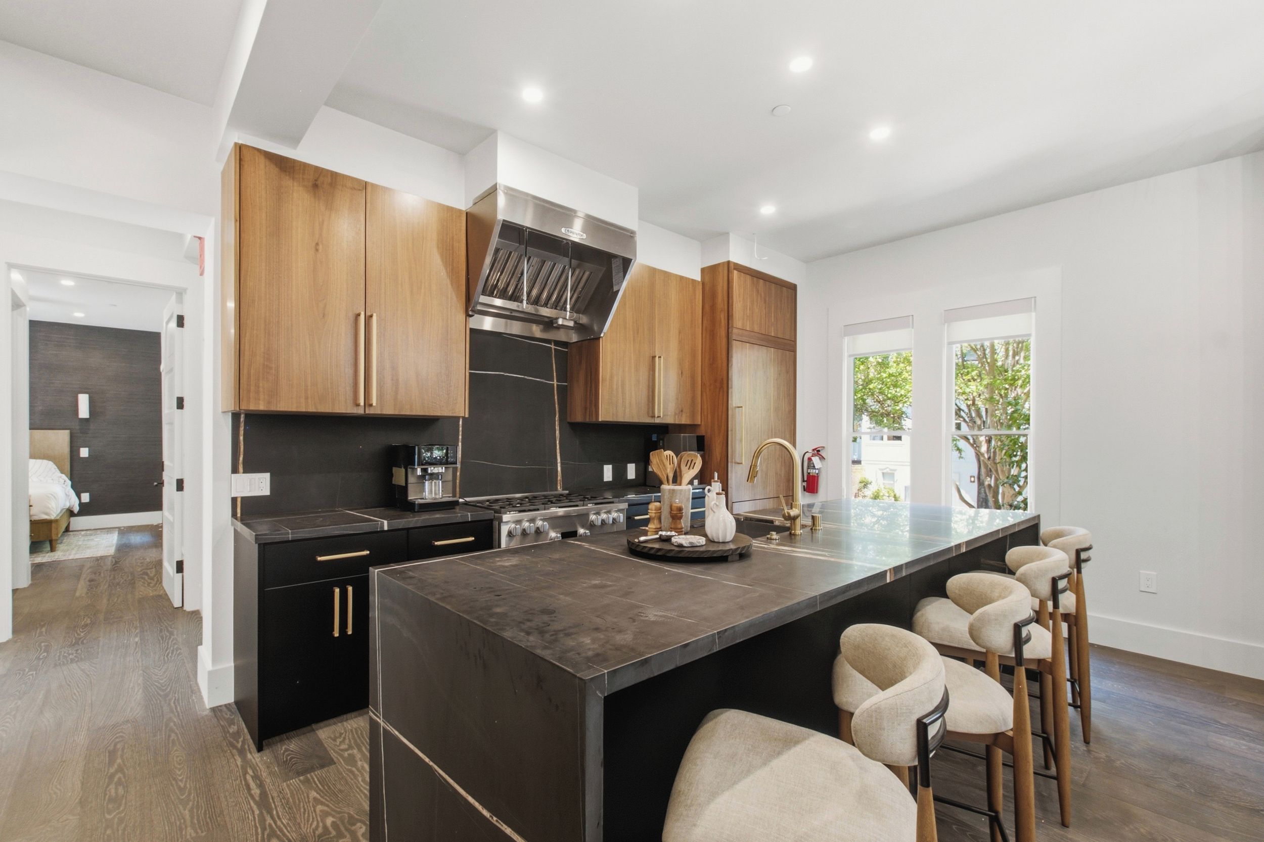 Una cocina moderna con armarios oscuros, una isla central con taburetes y vistas al exterior a través de amplios ventanales.