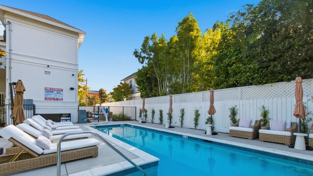 A swimming pool with lounge chairs and umbrellas, surrounded by a white fence and trees.