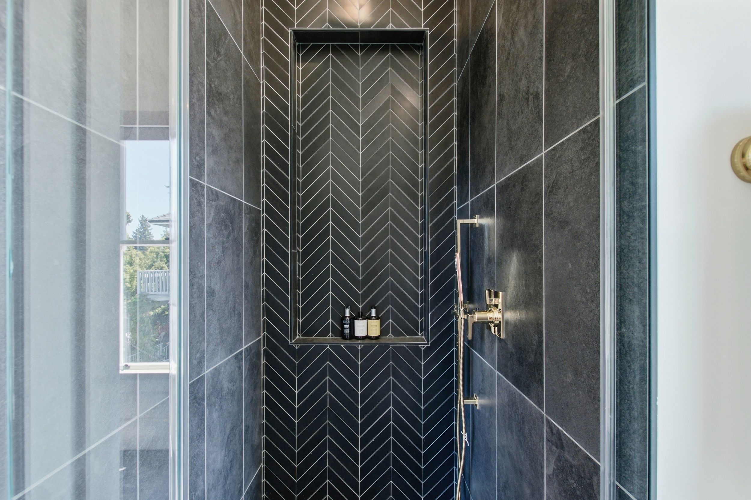 A modern bathroom with a black and white chevron tile pattern, a glass shower enclosure, and a visible window.