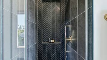 A modern bathroom with a black and white chevron tile pattern, a glass shower enclosure, and a visible window.