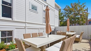 An outdoor patio with a white table and wicker chairs, a barbecue grill, and a white fence.