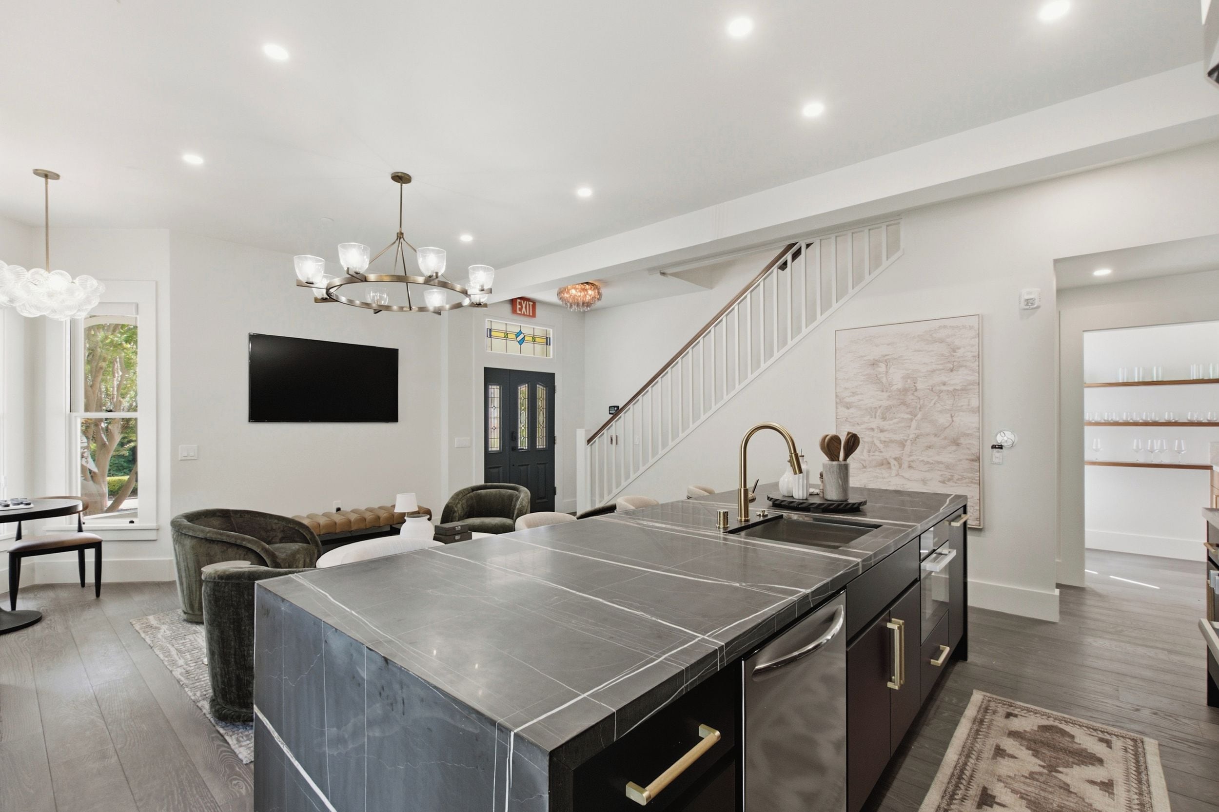 A modern kitchen with a large island, a dining area with a sofa, and a staircase leading to another level.