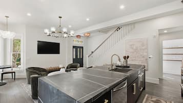 A modern kitchen with a large island, a dining area with a sofa, and a staircase leading to another level.